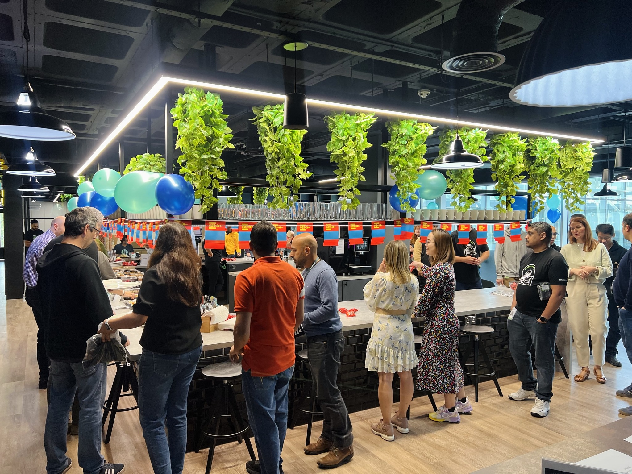 a group of people standing in a room with balloons and a bar