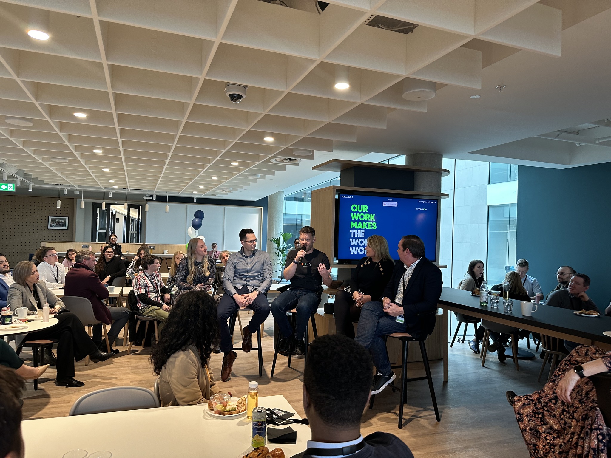 a group of people sitting in chairs in a room with a large screen